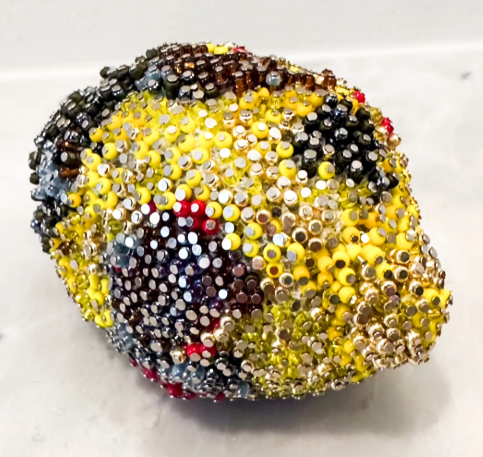 The beaded lemon from above, a bright yellow field crossed by a dark bruise of plum, amber and steel beads.