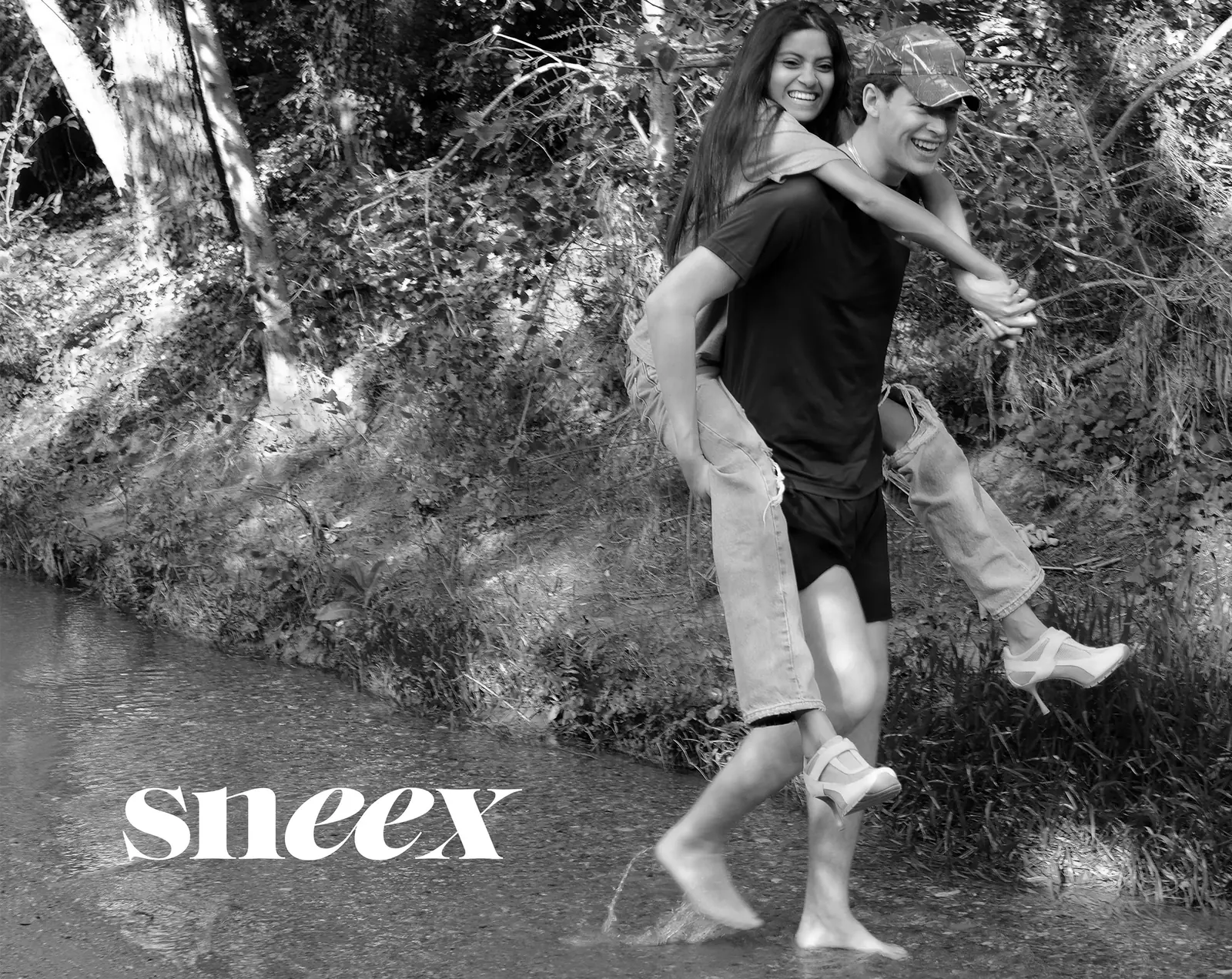Black and white: a piggyback carry beneath overhanging trees, with the Sneex wordmark at lower left.