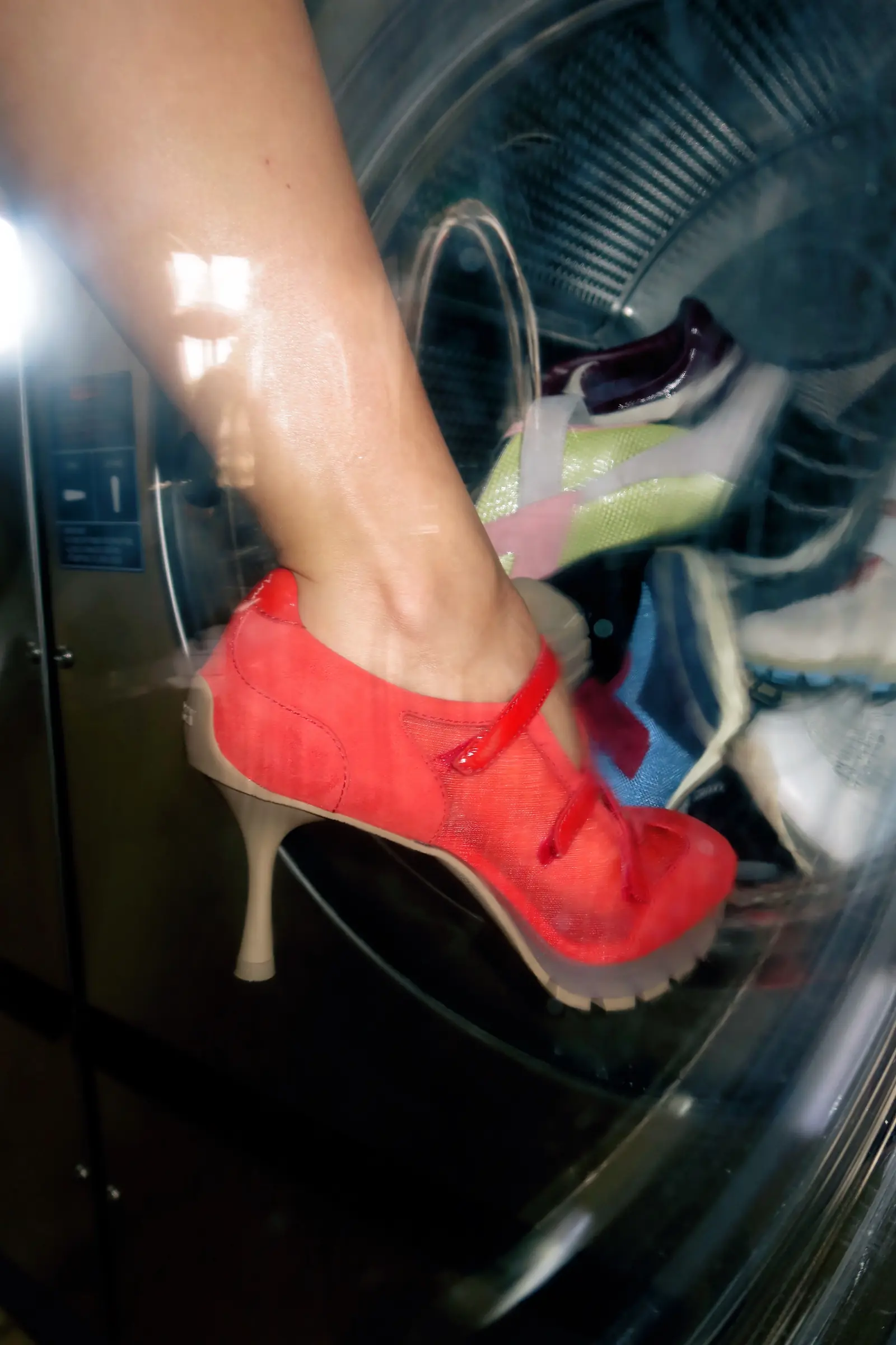 Close-up of a red mesh Sneex heel stepping into a washing machine drum full of shoes.