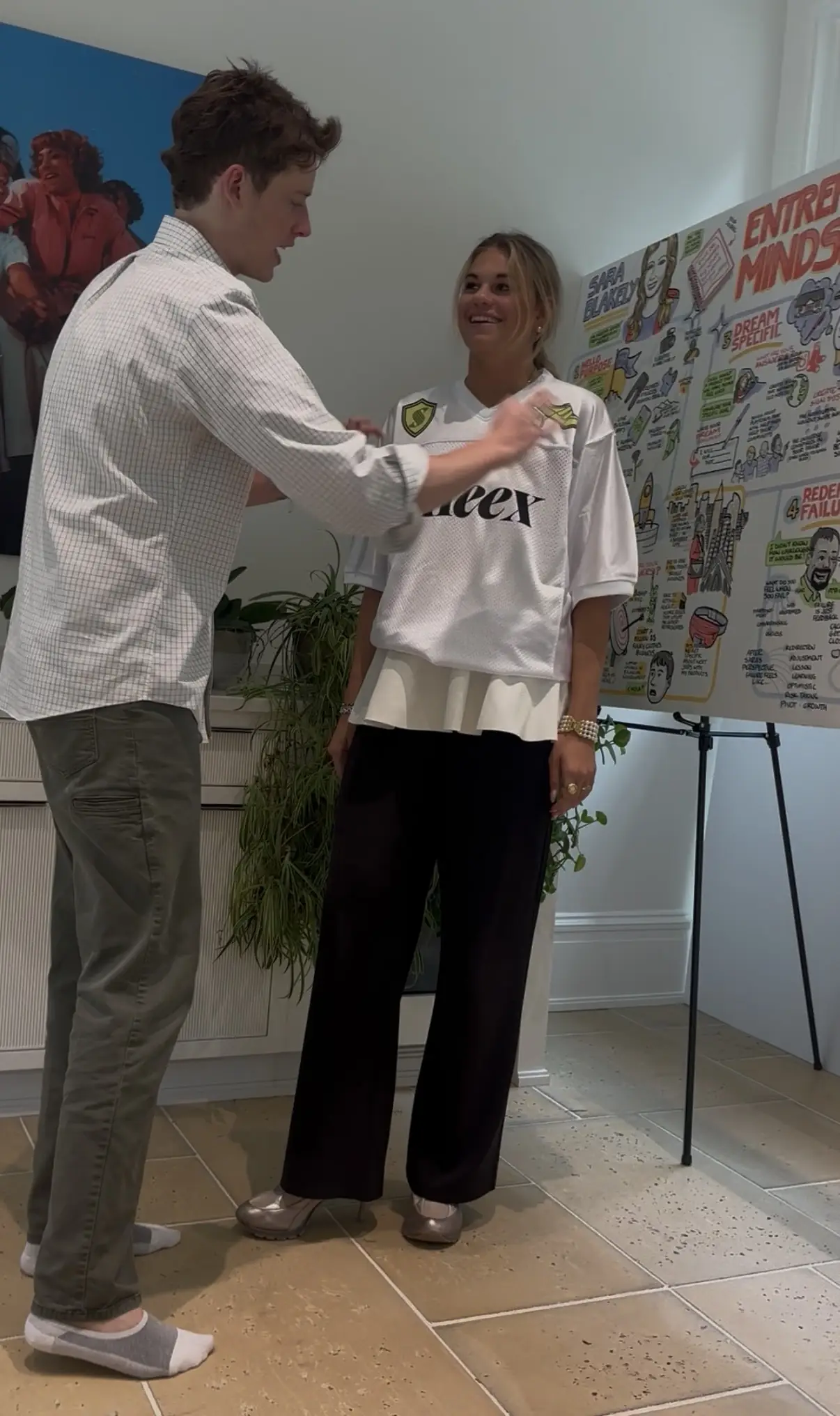 Henry adjusts the crest on a white Sneex jersey worn by a teammate, beside a wall of hand-drawn strategy boards.