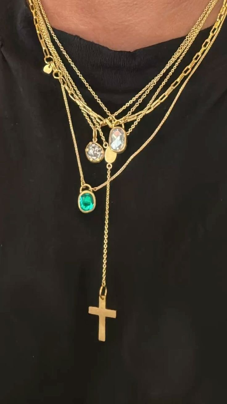 Layered gold necklaces with crystal and emerald pendants and a gold cross over a black T-shirt, pinned as a jewelry reference.